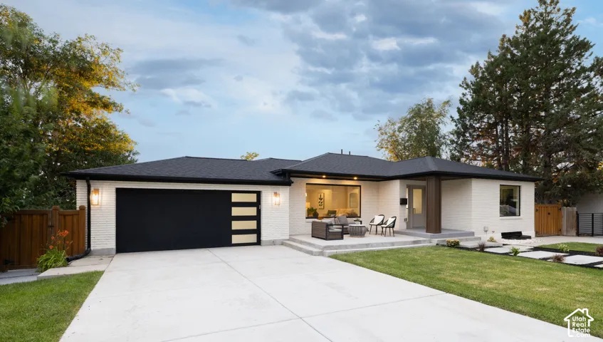 Contemporary ranch-style residence featuring a white brick exterior, a black shingle roof, and a large concrete driveway