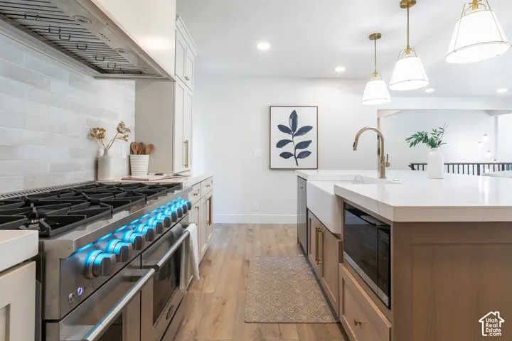 Gourmet kitchen with professional-grade stainless steel range, white subway tile backsplash, white shaker cabinetry, large center island with farmhouse sink, and wood-finish flooring