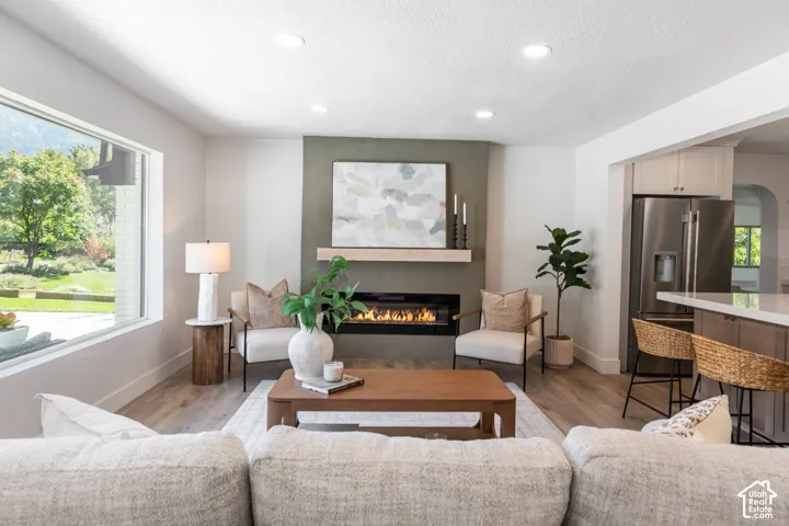 Recessed lighting, a gas fireplace with a light wood mantle, wood-finish flooring, a stainless steel refrigerator, and built-in cabinetry