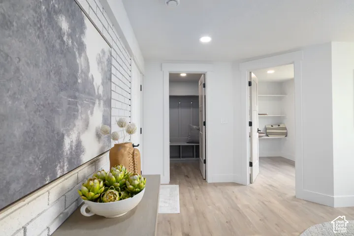 Hallway featuring light wood-finish flooring, white trim, recessed lighting, and a white brick-style accent wall