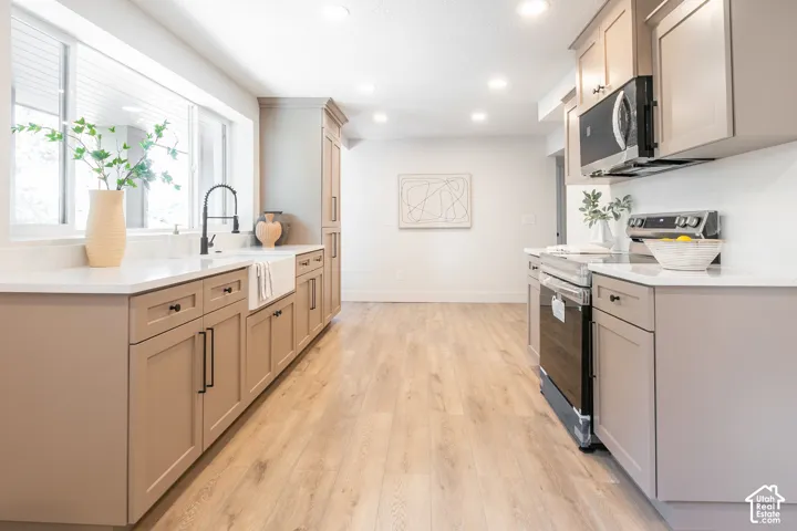 Modern kitchen featuring wood-finish flooring, two-tone cabinetry with black hardware, a farmhouse-style sink, and stainless steel appliances