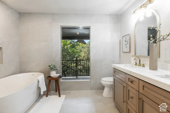 Freestanding soaking tub, wood-finish double vanity with dual sinks, overhead vanity lighting, and full wall tile surround