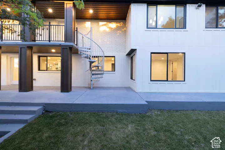 Exterior showcasing a white spiral staircase, upper-level balcony with dark railings, and a concrete patio