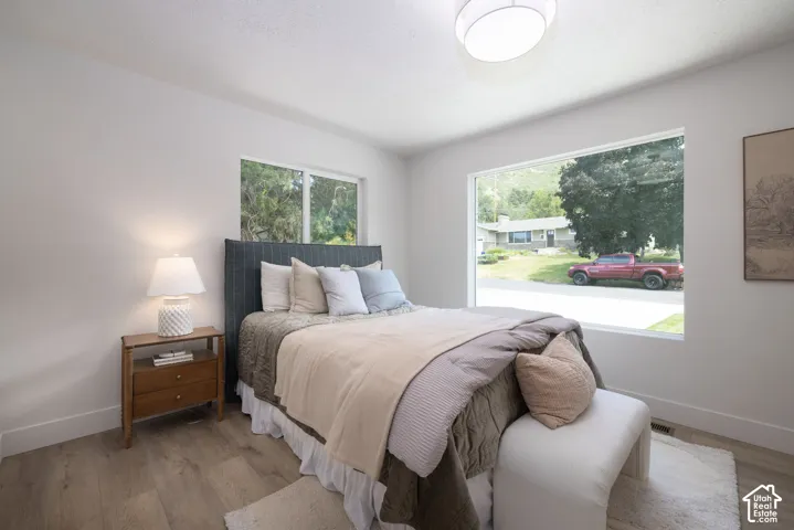 Bright room featuring a large picture window, wood-finish flooring, white baseboards, and a semi-flush mount ceiling light