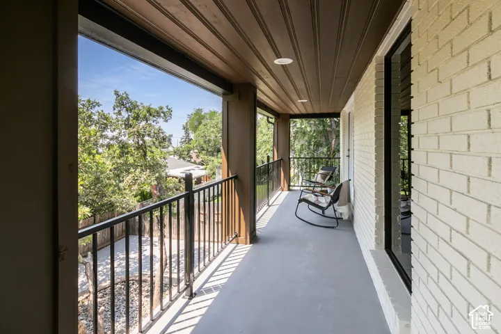 Covered outdoor balcony featuring white brick siding, dark wood-finish ceiling, recessed lighting, and black metal railings