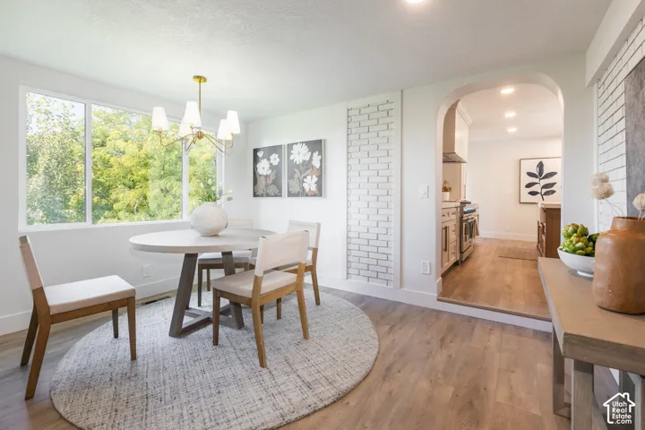 Spacious dining area featuring wood-finish flooring, a large window, a modern chandelier, and a decorative white brick accent wall