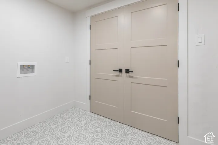 Dual panel doors with matte black hardware, patterned floor tile, white baseboards, and a recessed utility box