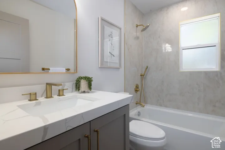 Bathroom featuring a white bathtub with gold-finish fixtures, a window, and large format wall tiling