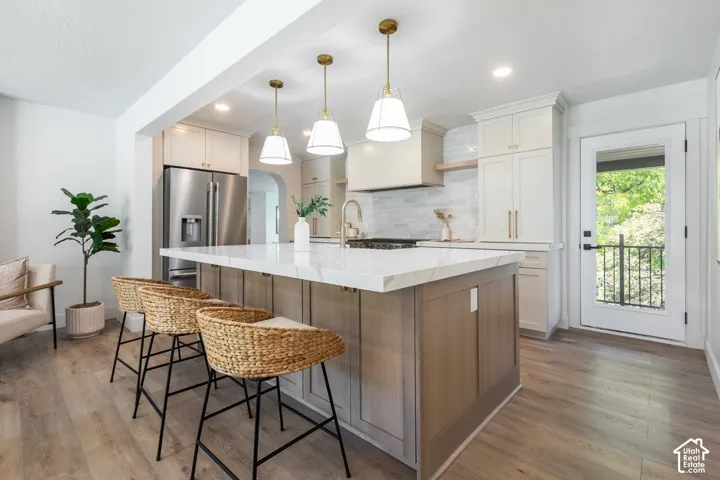Kitchen featuring a center island with a stone countertop, wood-finish flooring, white cabinetry, a built-in stainless steel refrigerator, and a glass-paneled door with an iron railing