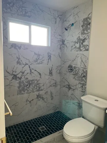 Walk-in shower with large format marble-look tile walls, black subway tile floor, and a chrome shower head
