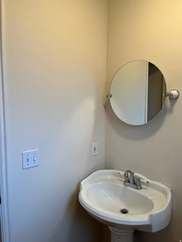 Pedestal sink with chrome-finish faucet and a wall-mounted circular mirror