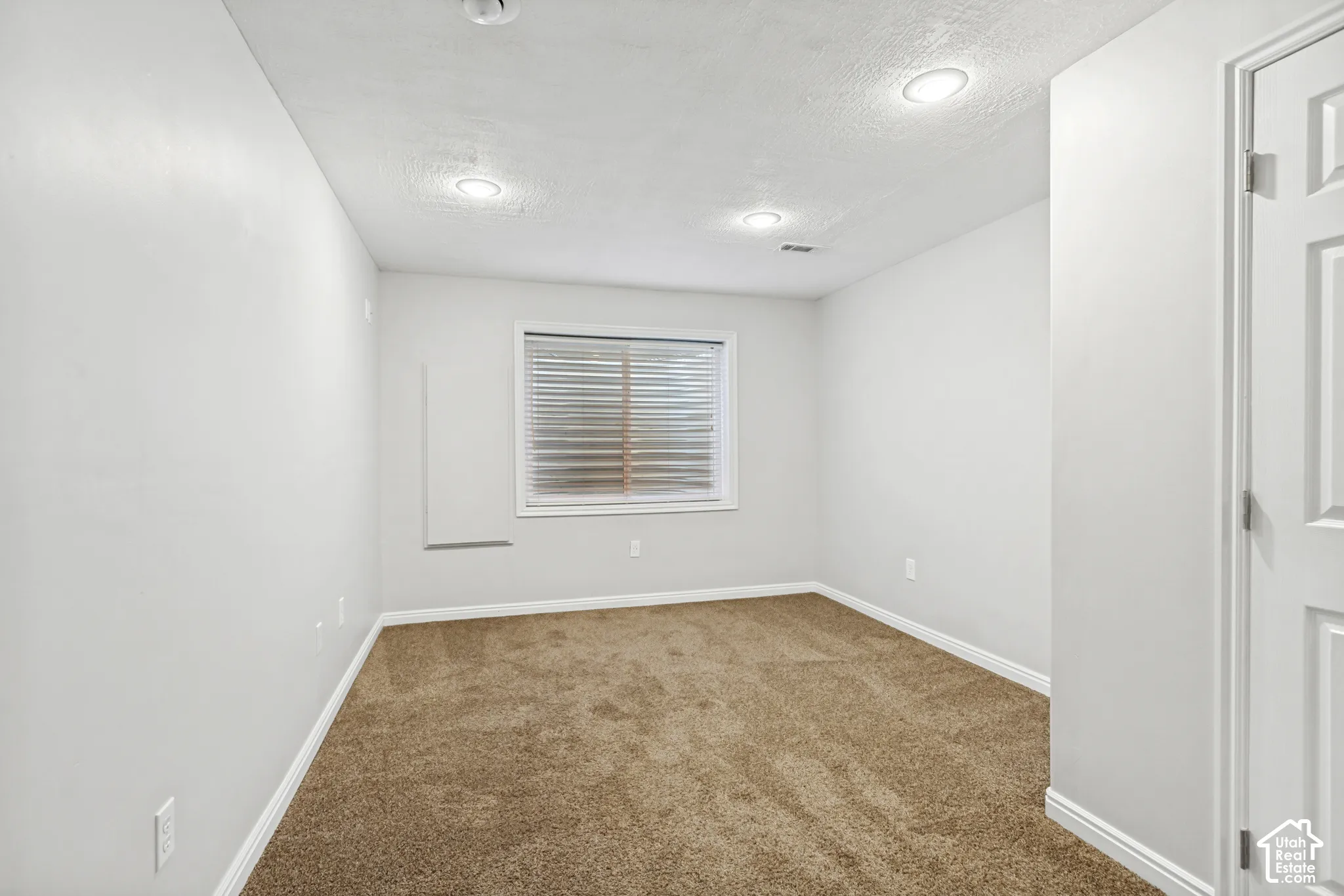 Interior room featuring light gray walls, brown carpet, recessed ceiling lighting, a window with horizontal blinds, and a white interior door