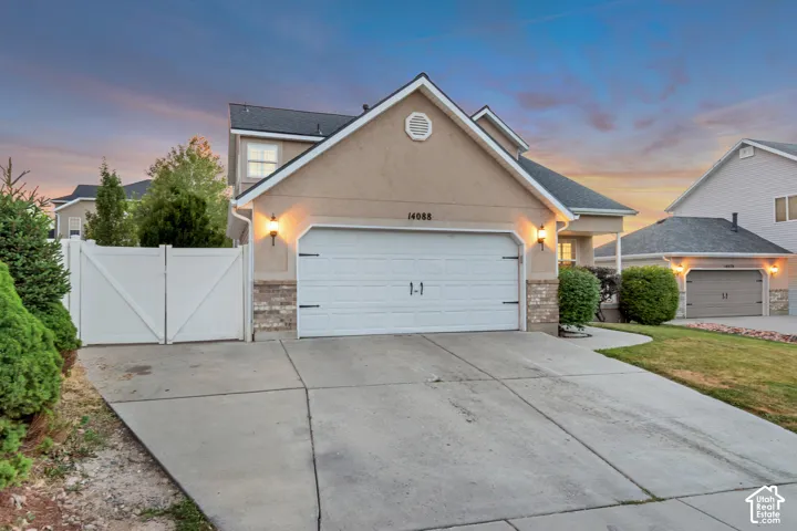 Stucco exterior featuring a dual garage door, stone veneer accent, and exterior wall sconces