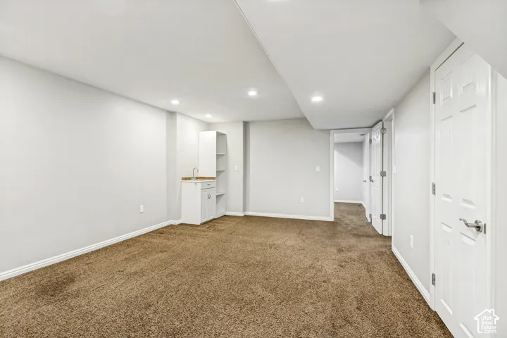 Recessed lighting illuminates this space featuring light gray walls, brown carpet, and white baseboards