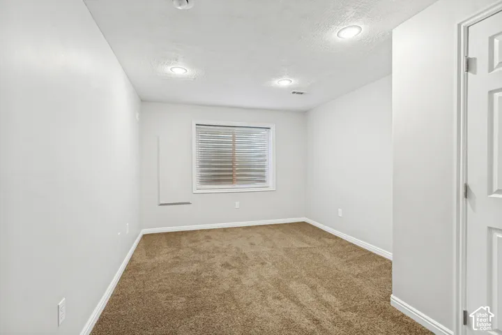 Interior room featuring light gray walls, brown carpet, recessed ceiling lighting, a window with horizontal blinds, and a white interior door