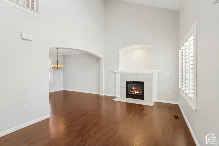 Spacious living area featuring a fireplace with a tile surround and mantel, rich wood-finish flooring, and high ceilings