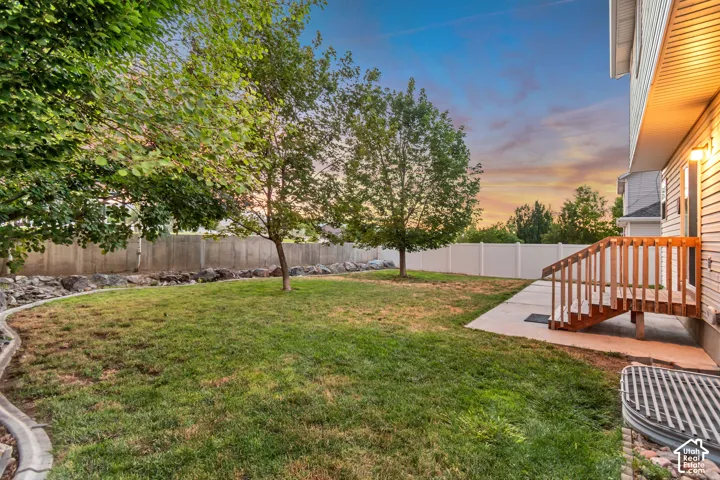 Generous backyard featuring mature trees, a concrete patio, and a wood deck with stairs