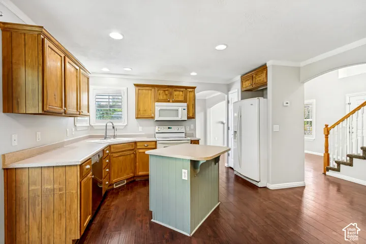 Kitchen featuring wood cabinetry, white appliances, light countertops, a central island with a contrasting base, and wood-finish flooring