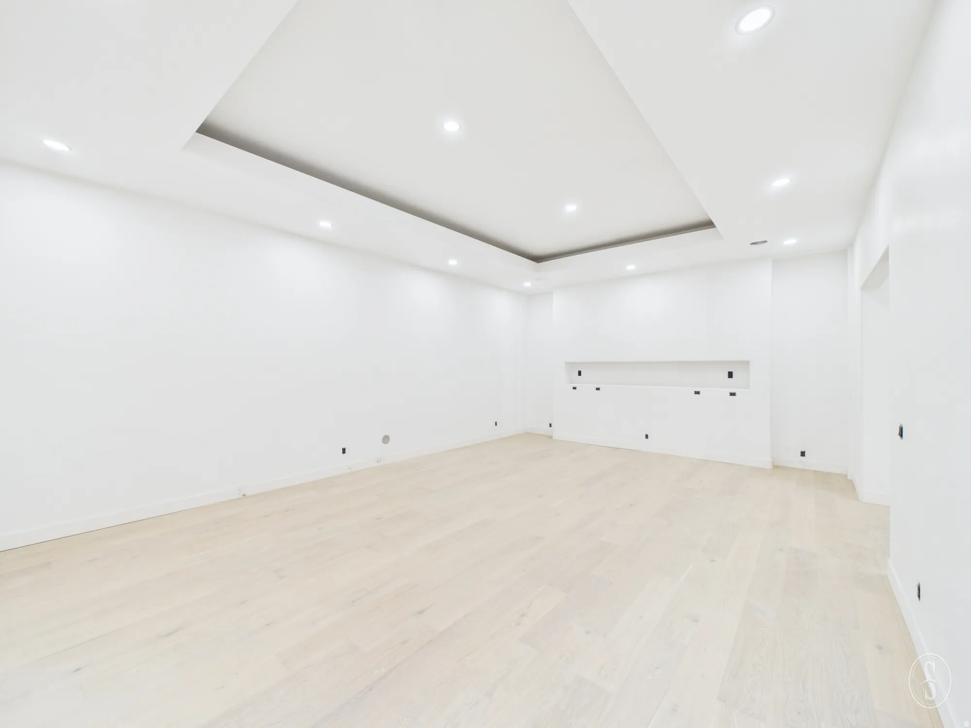 Spacious room featuring light wood-finish flooring, recessed lighting, and a tray ceiling design