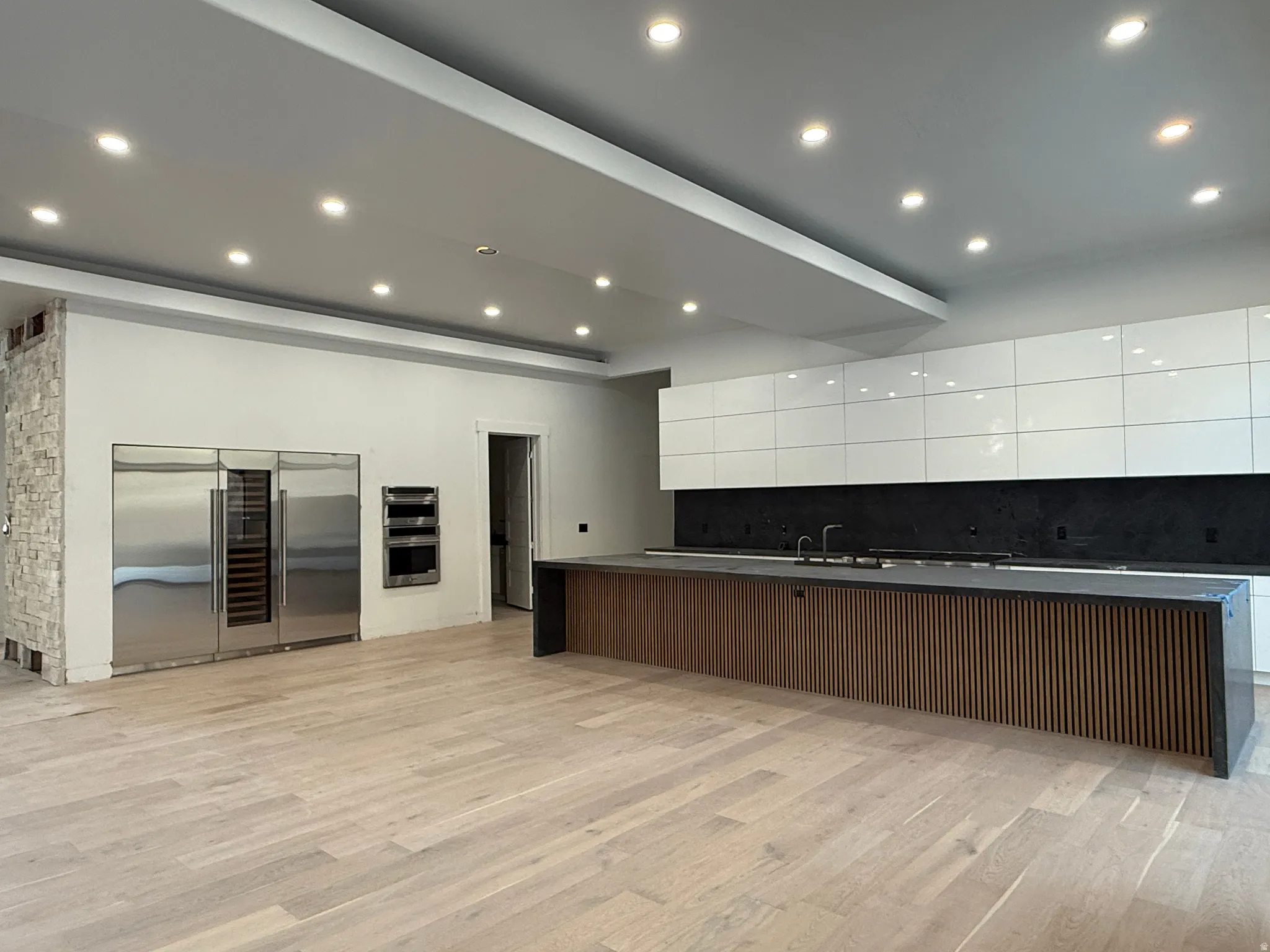 Recessed lighting, wood-finish flooring, stainless steel appliances, kitchen island with built-in sink, and white flat-panel cabinetry