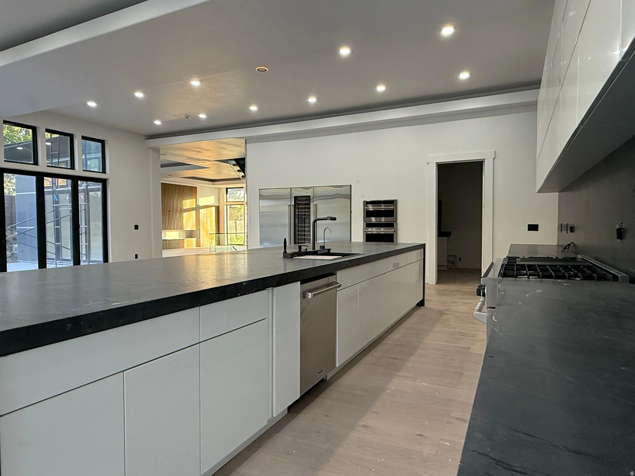 Spacious kitchen featuring a large island with an integrated sink, stainless steel dishwasher, modern white cabinetry, and recessed lighting