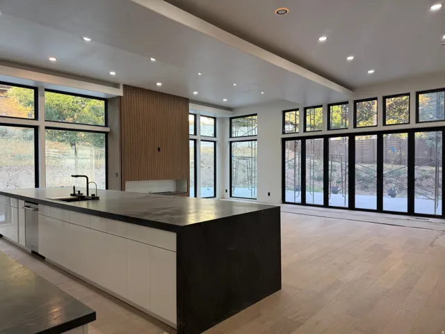 Spacious interior featuring wood-finish flooring, a contemporary kitchen island with a dark countertop and integrated sink, abundant natural light from extensive windows, and recessed ceiling lighting