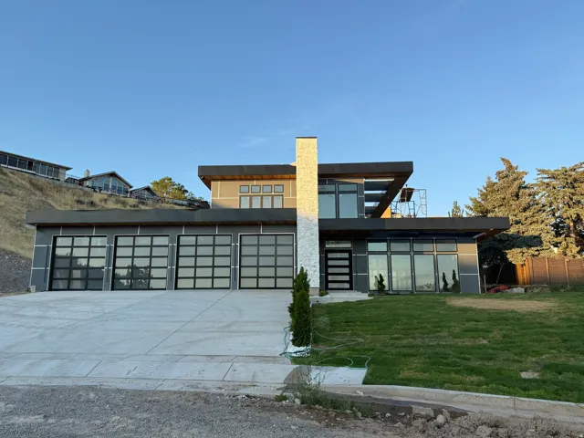 Modern architectural design with a prominent stone-clad vertical element, multi-panel garage doors, and an expansive concrete driveway