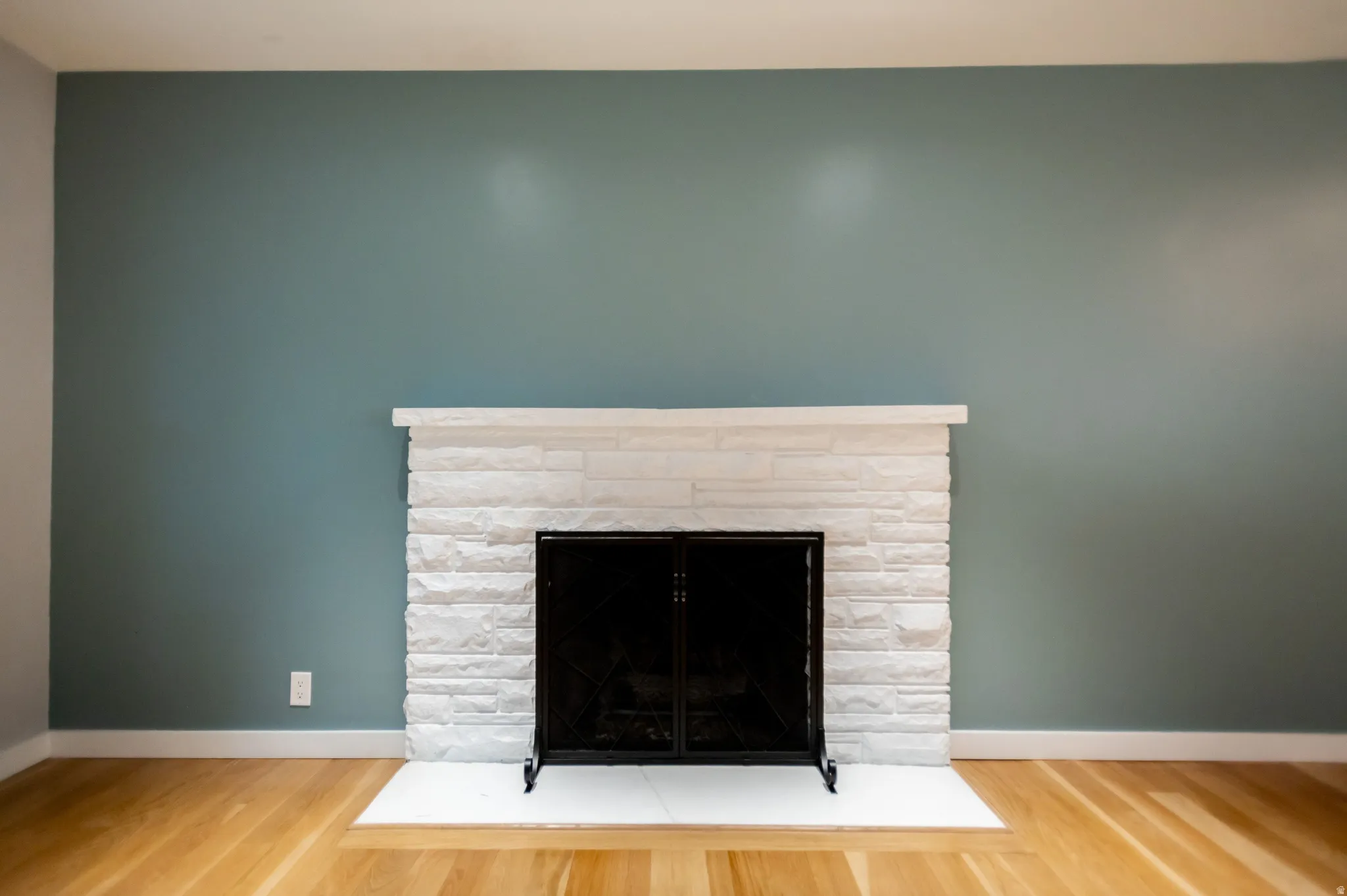 Fireplace featuring a white stacked stone surround, a black metal screen, and a white hearth