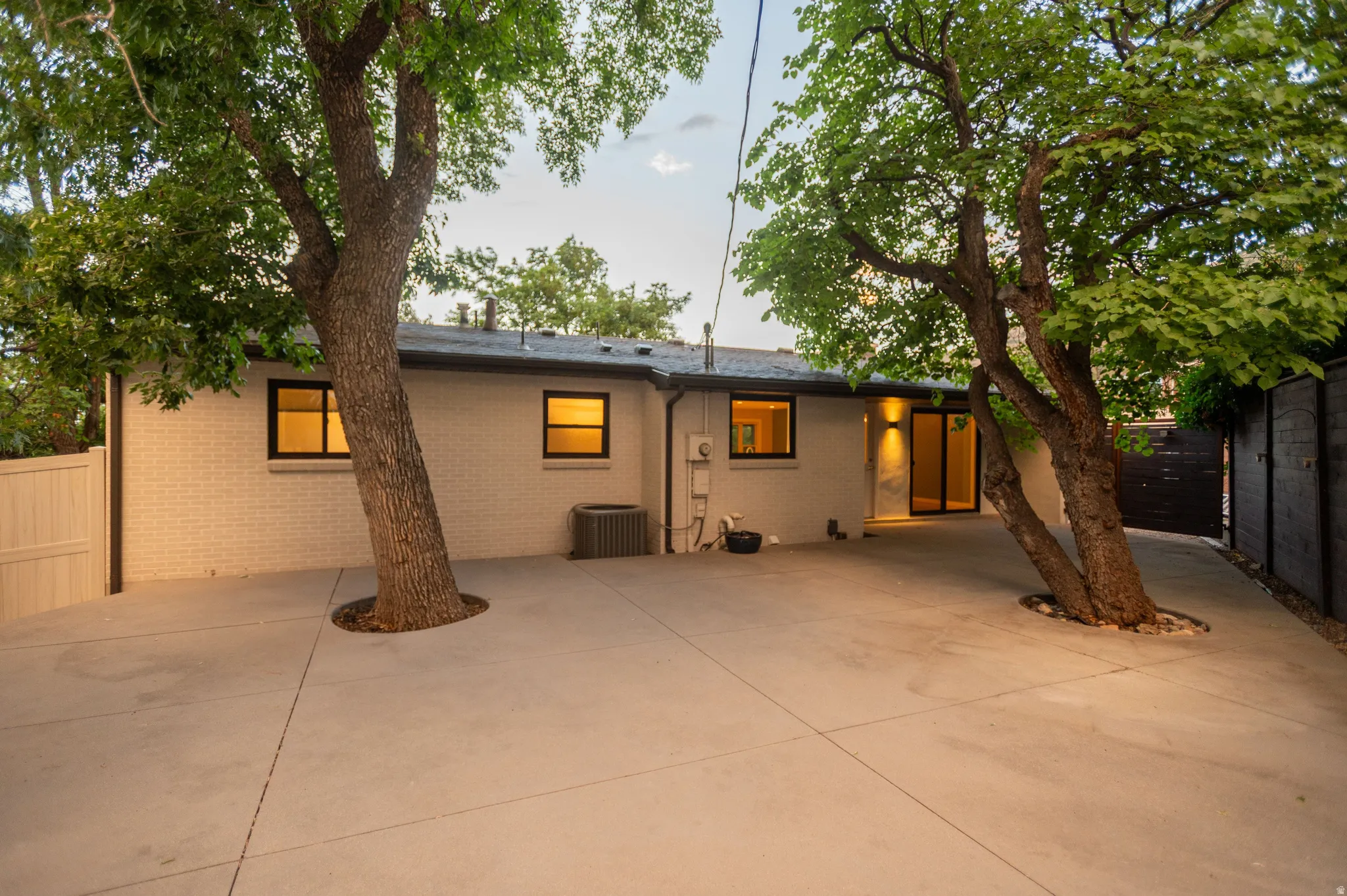 Expansive concrete patio area with mature trees and a white brick exterior