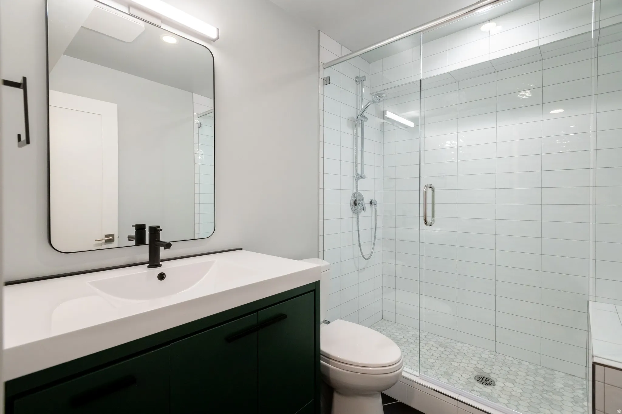 Modern bathroom featuring a dark green vanity with an integrated white sink, matte black faucet, and a large frameless mirror