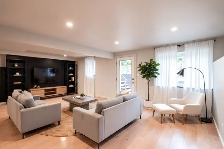 Light wood-finish flooring complements white walls and recessed lighting in this living space. Virtually staged
