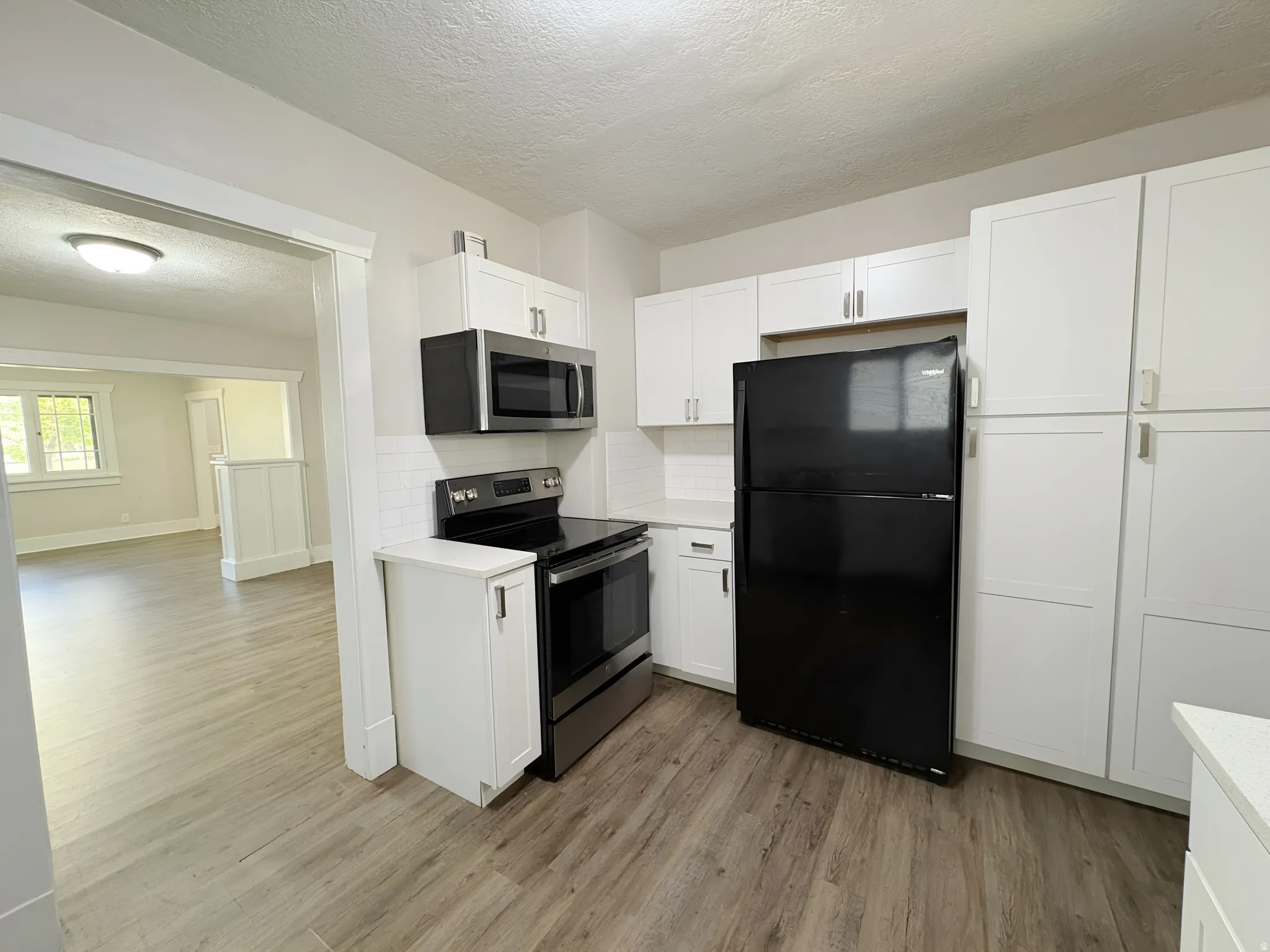 Kitchen featuring white shaker-style cabinetry, stainless steel appliances, a white subway tile backsplash, light-toned countertops, and wood-finish flooring