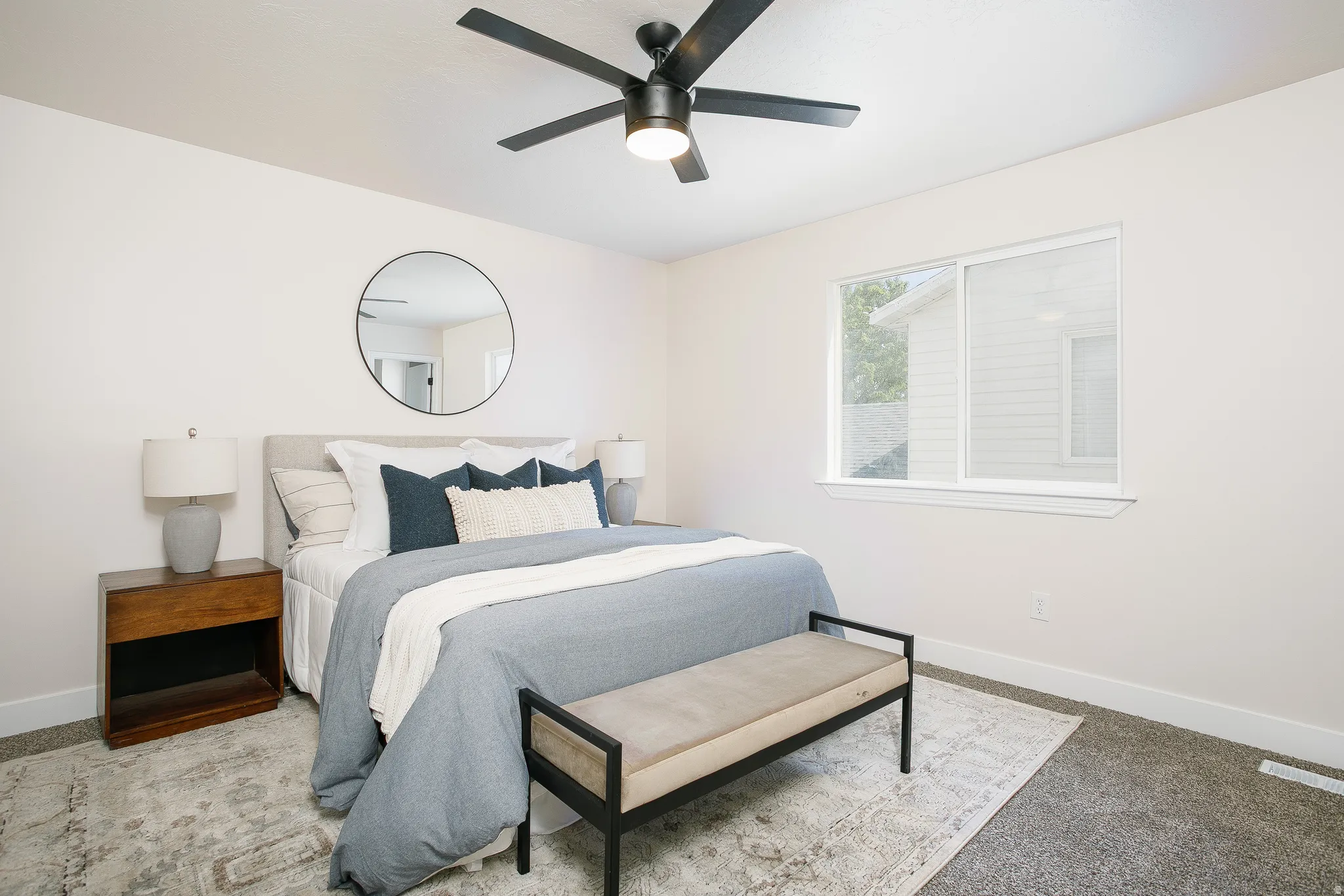 Bedroom featuring light-colored walls, carpeted flooring, and a large window providing ambient light