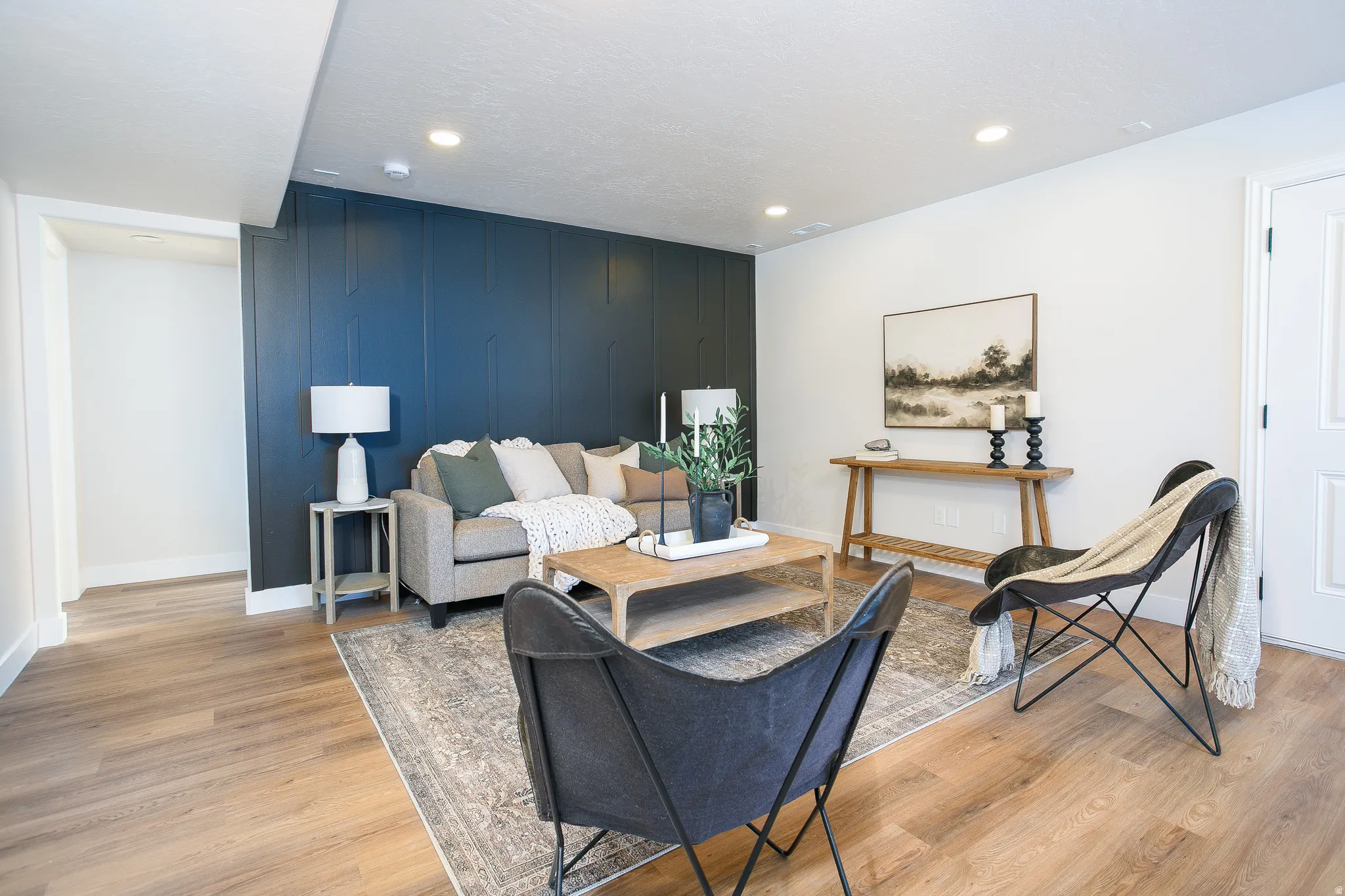 Living area featuring a dark accent wall with vertical paneling, light wood-finish flooring, recessed ceiling lighting, and a white interior door