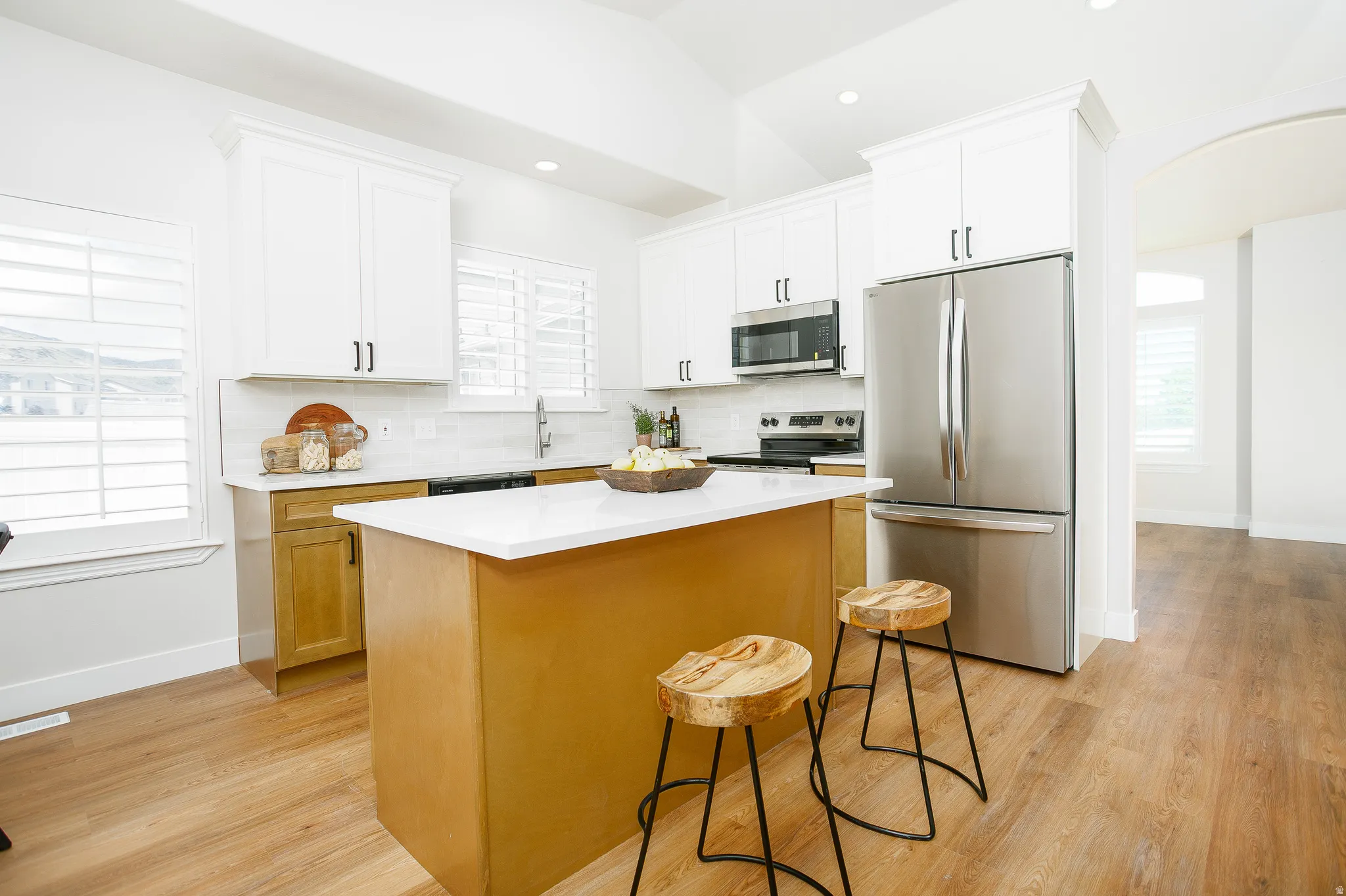 Modern kitchen featuring a central island with a white countertop, two-tone cabinetry, stainless steel appliances, a tile backsplash, and wood-finish flooring