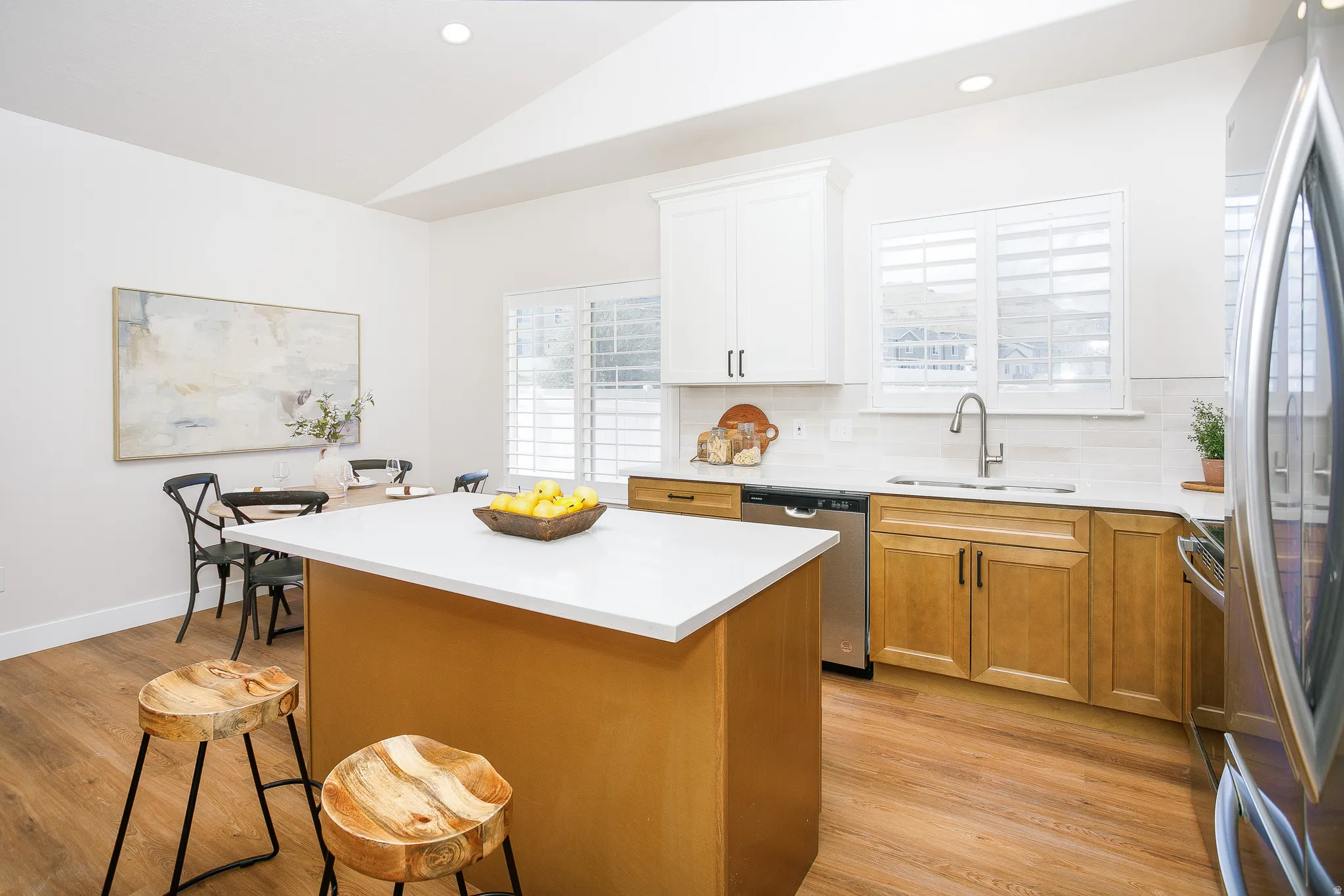 Kitchen featuring a central island with white countertop, stainless steel appliances, wood-finish flooring, white cabinetry, and a tile backsplash