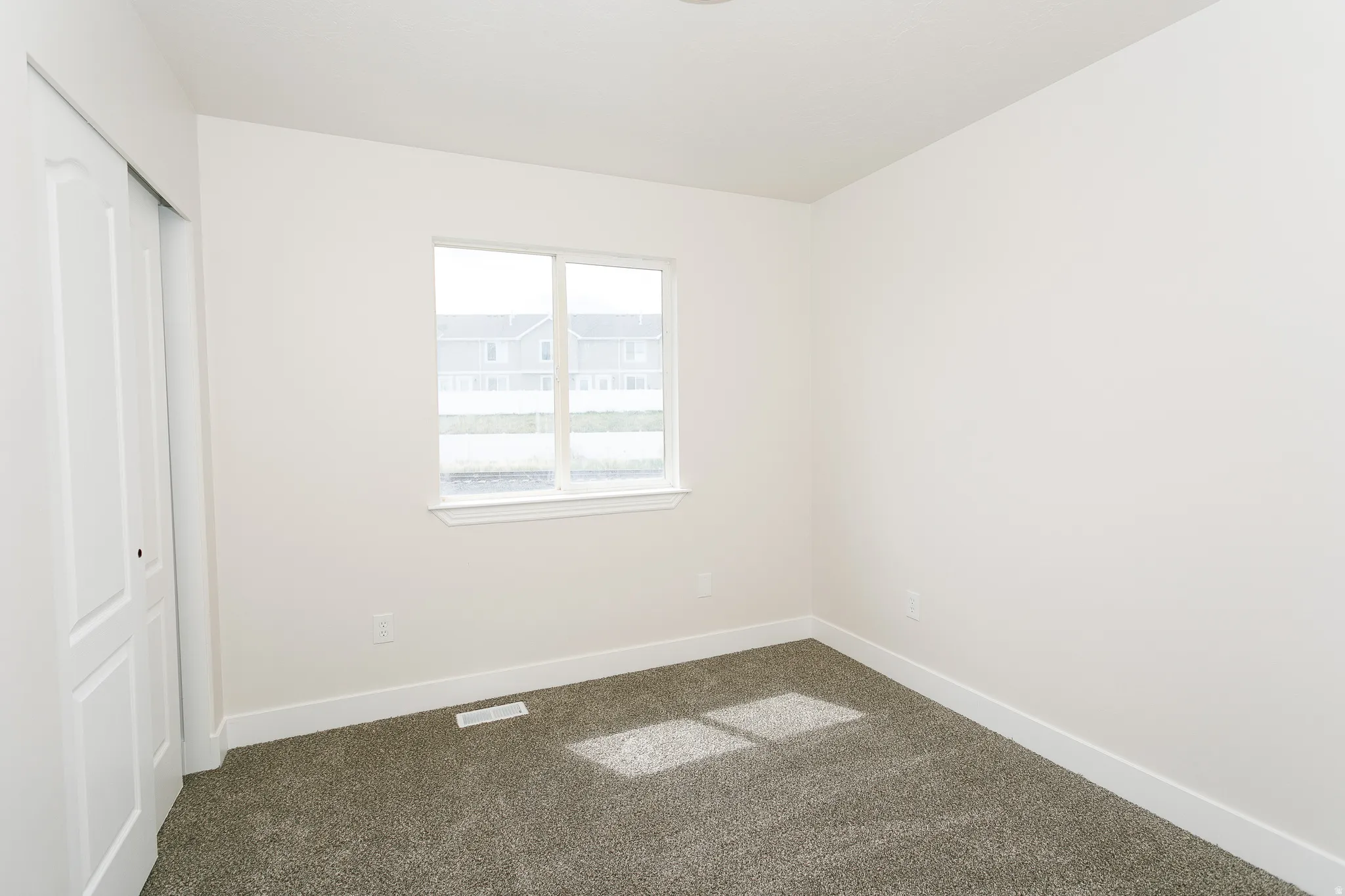 Room featuring a double-pane window, white trim, grey carpet, and a sliding closet door