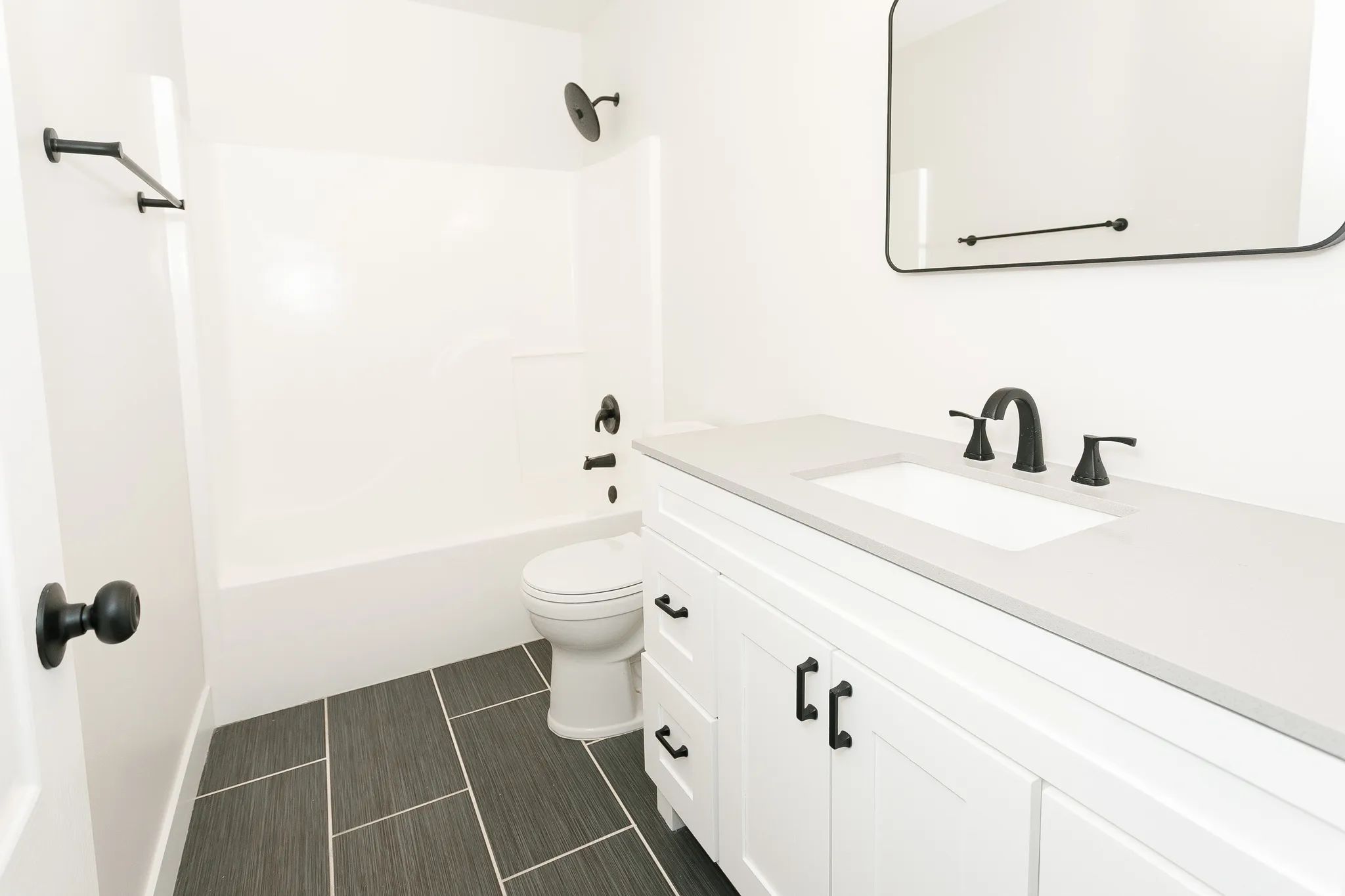 Bathroom featuring dark gray rectangular floor tiles, a white vanity with a light gray countertop, a rectangular undermount sink, and matte black fixtures