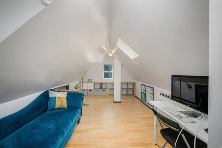 Attic room featuring bright white walls, skylight, wood-finish flooring, and built-in shelving