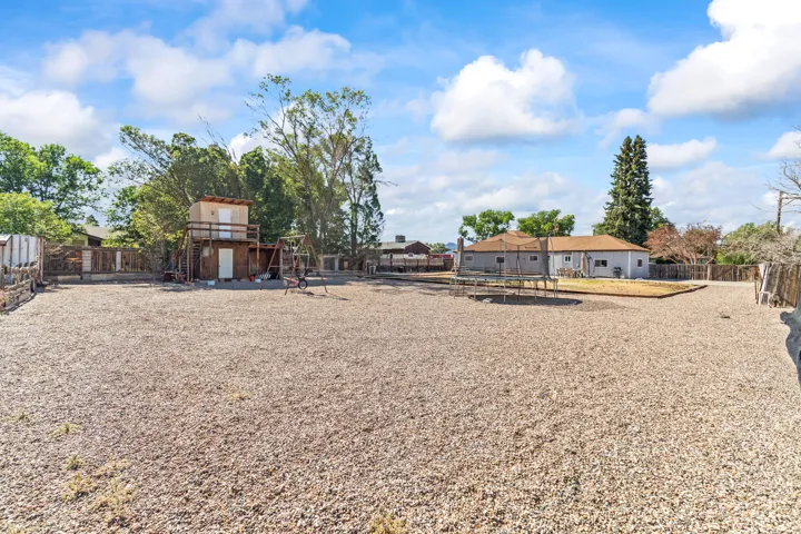 Expansive gravel yard featuring a multi-level outdoor structure and perimeter fencing