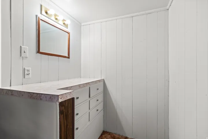 Built-in vanity with a stone-finish countertop, six drawers, and an overhead mirror with a four-bulb light fixture
