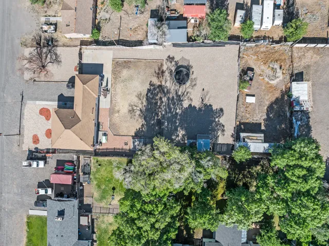 Expansive property featuring a large gravel lot, a substantial building with a brown roof, paved driveways, a fenced perimeter, and mature trees providing natural shading