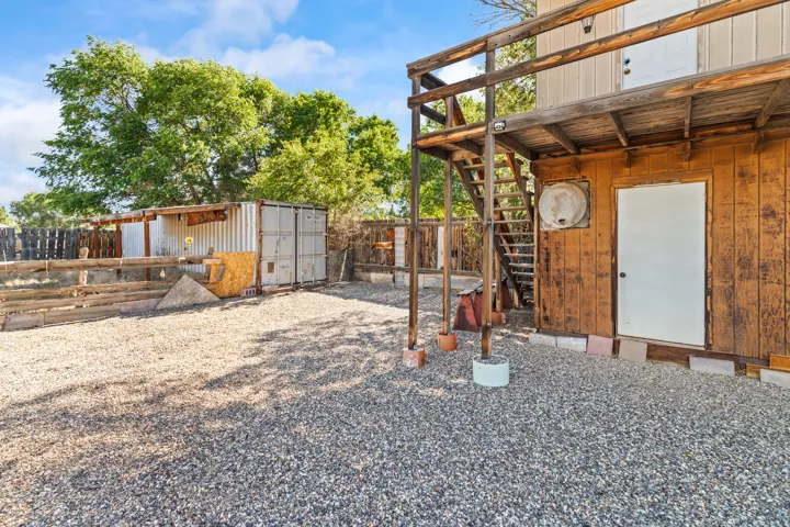 Gravel-covered outdoor space featuring a two-story wooden structure with an exterior staircase and an upper-level balcony