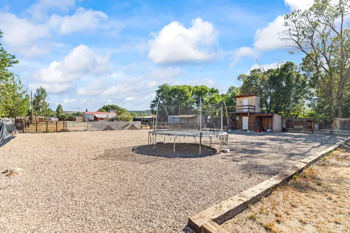 Expansive gravel-covered outdoor area featuring perimeter fencing, mature trees, and a multi-level outbuilding