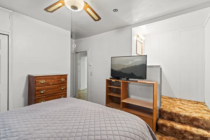 White-painted interior space featuring a ceiling fan with integrated lighting, flat white walls, and a white paneled door