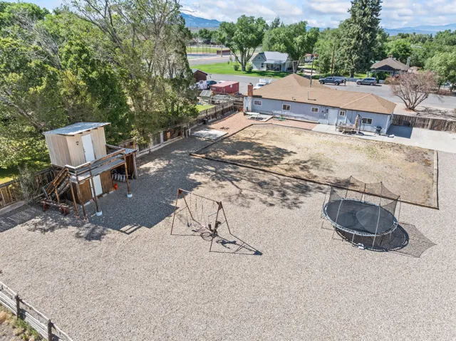 Expansive gravel yard featuring a multi-level play structure, swing set, and a designated grass area