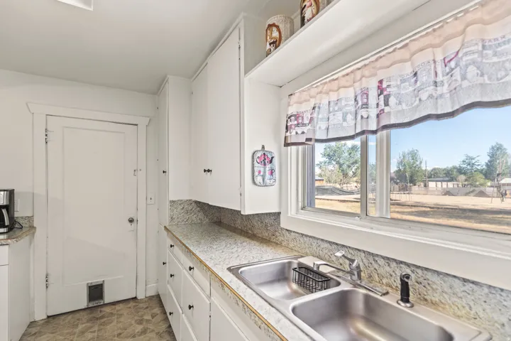 Kitchen features a double basin stainless steel sink, white cabinetry with dark hardware, and light-colored countertops with a textured finish