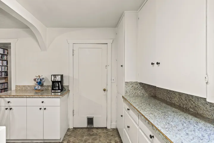 Functional kitchen area with white cabinetry, speckled countertops, and patterned flooring