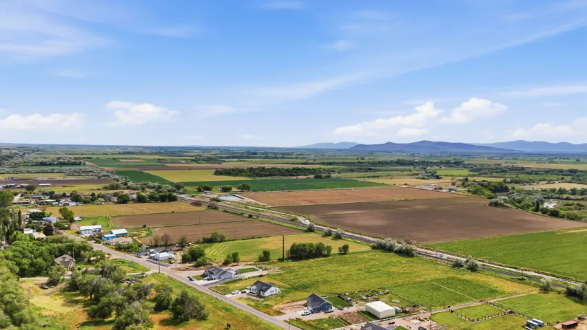 Expansive agricultural landscape featuring diverse fields of green and brown, framed by distant mountains under a blue sky with scattered clouds