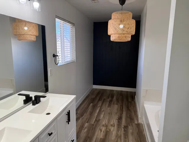 Modern bathroom featuring wood-finish flooring, a white dual vanity with matte black fixtures, and a large mirror